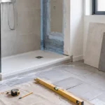 Baño en reforma con plato de ducha, mampara, azulejos y herramientas